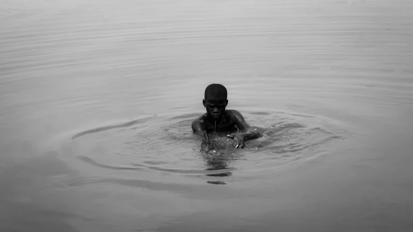 person wearing black swims through the water of a lake