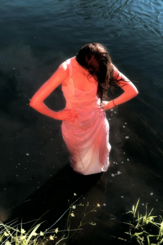 a young lady in a sheer dress stands and looks out into the water