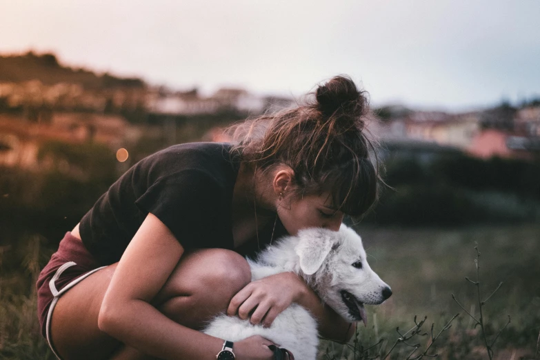 a woman holds a small dog as she kneels on the ground