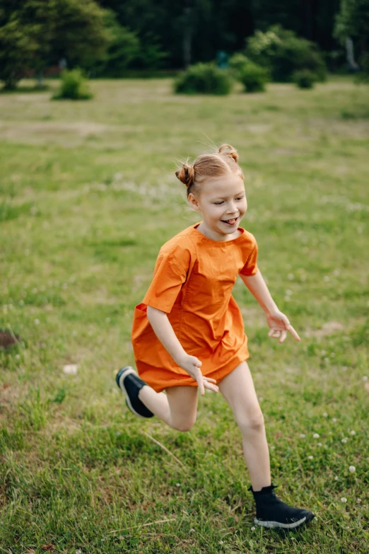 a child in an orange shirt runs across grass