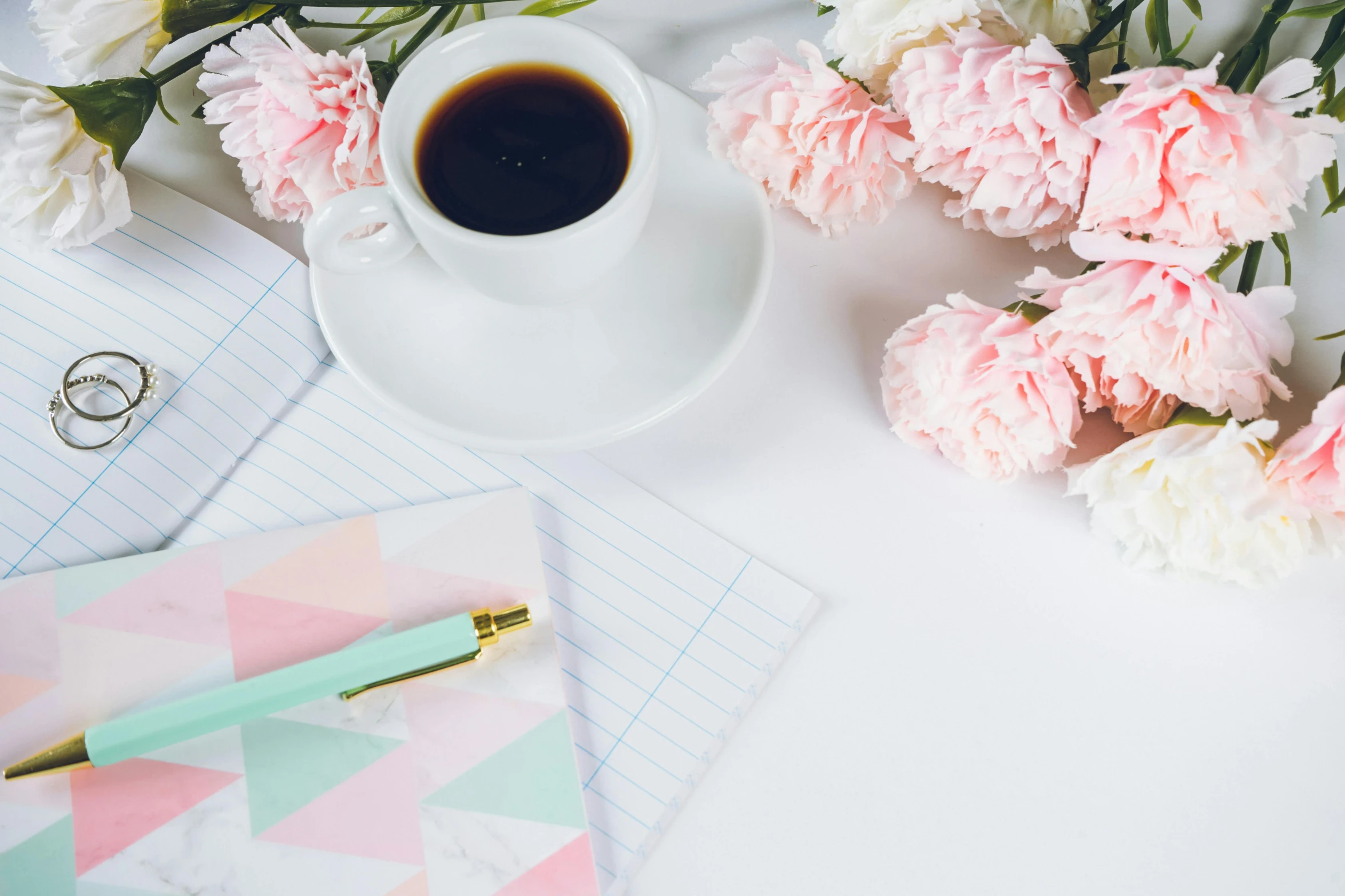 pink carnations, gold pens, and cup of coffee on a white desk