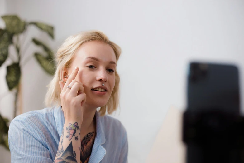 a woman wearing a blue shirt is looking at her face with a large amount of tattoo on it