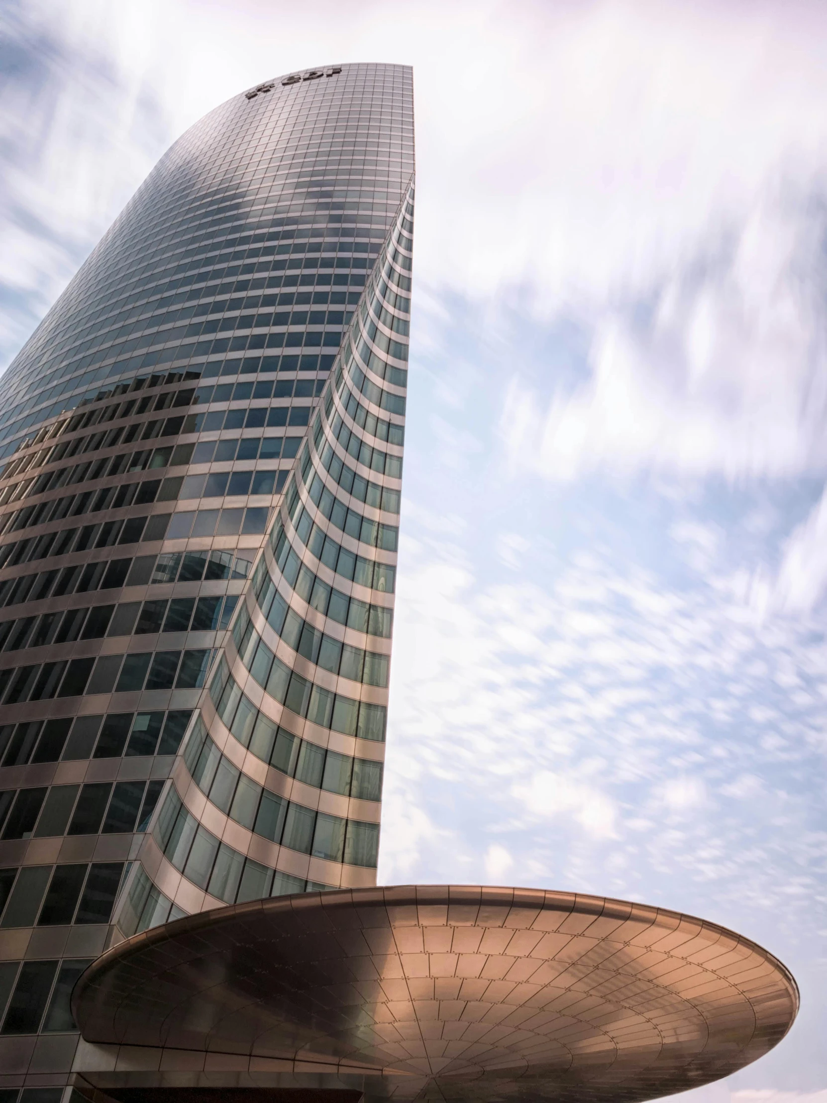 a very tall glass building next to a cloudy blue sky