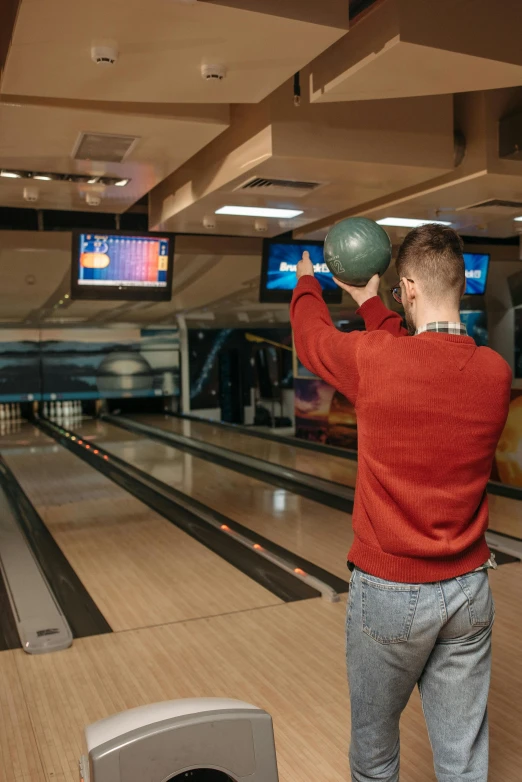 a man standing on a bowling court holding his arms up with the ball toward him