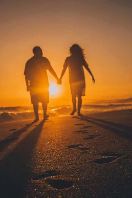 couple walking along beach holding hands as the sun sets