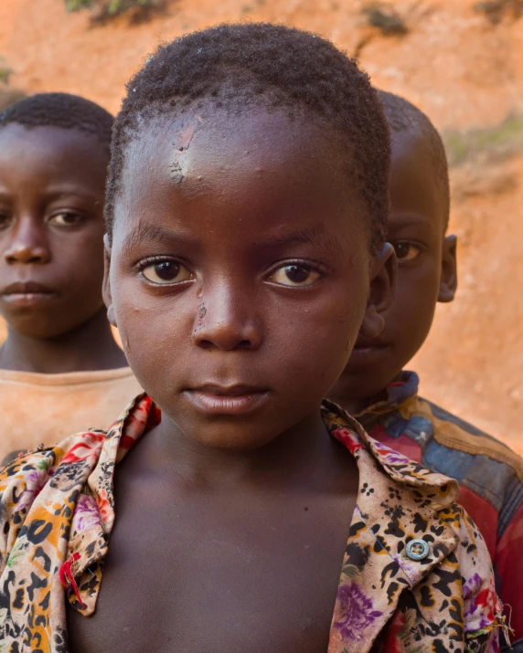 three young children standing close together in front of a rock