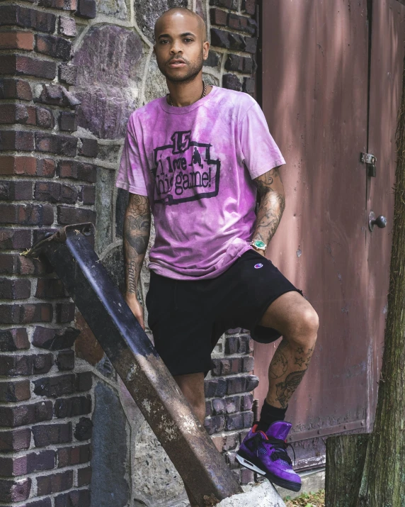 a man wearing purple t - shirt leaning against wooden railing