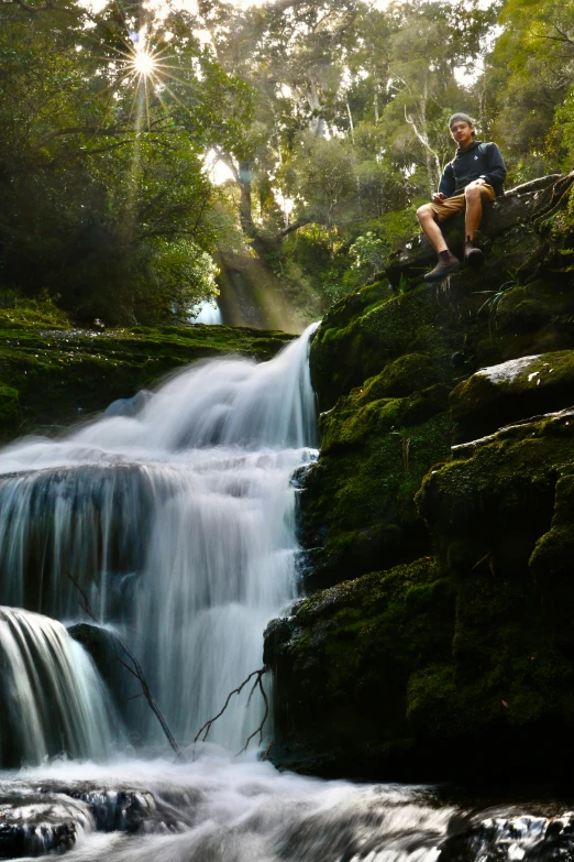 a man sits at the edge of a waterfall as it pours