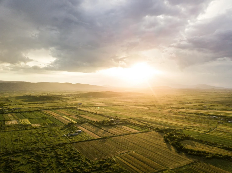 the sun rising behind some clouds above a big field