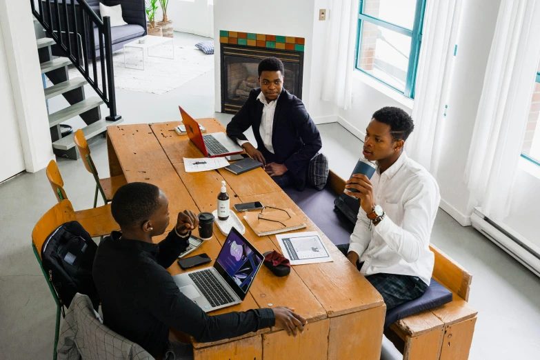 three men sitting at a table in front of laptops