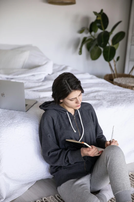 the girl is sitting on the bed writing on her notebook