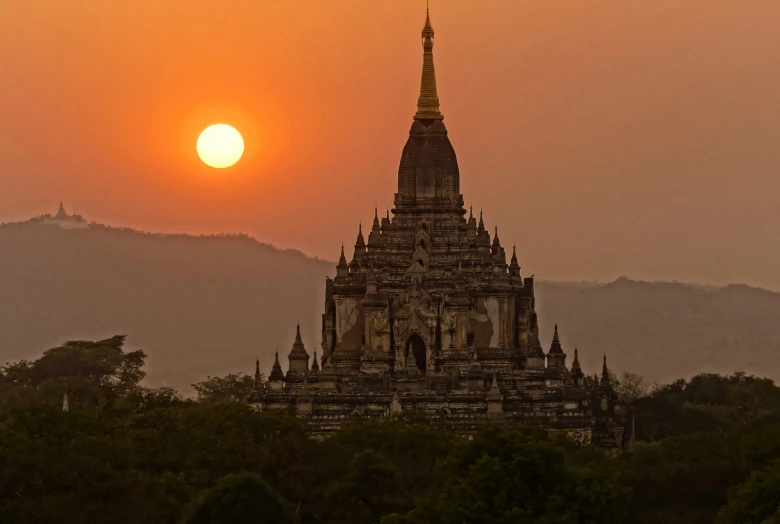 the sun rising over a very tall cathedral in myanmar