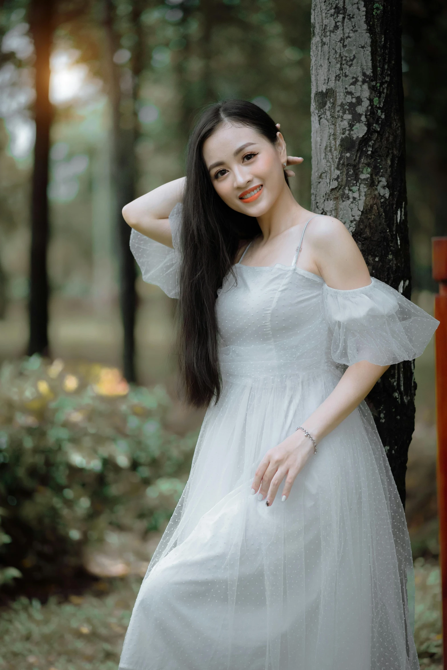 young woman in white dress standing next to tree