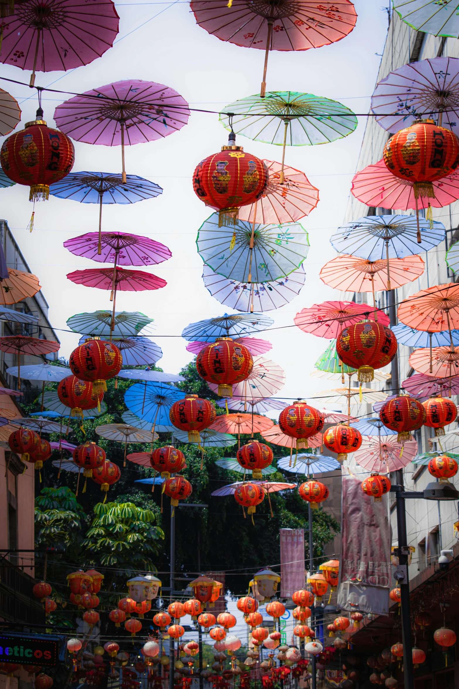 many colored umbrellas are attached to wires in this city