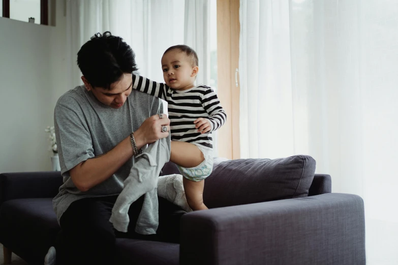 a person sitting on a couch while holding a baby and playing with soing