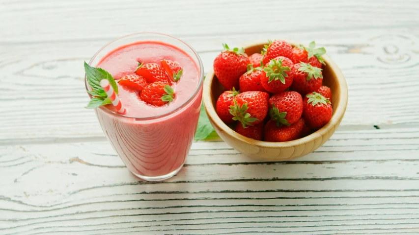 a bowl of strawberries next to a glass of smoothie