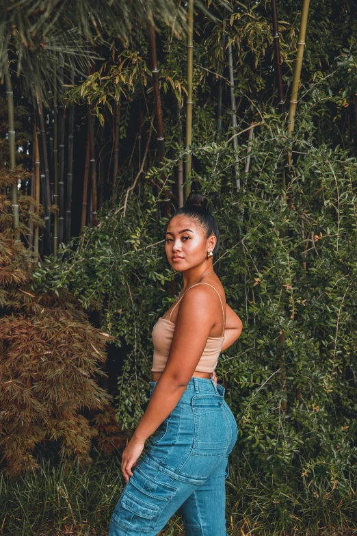 a woman with a tank top stands in the grass near the trees