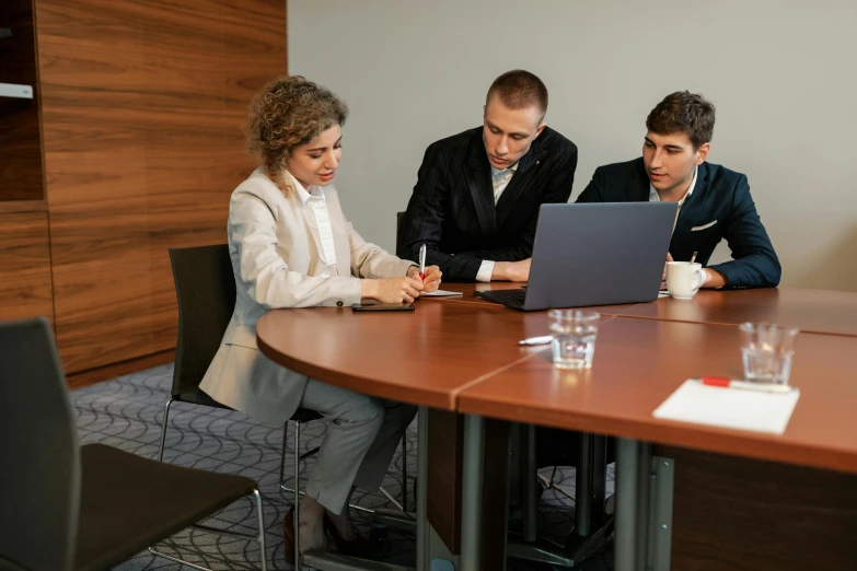 three people sitting at a table looking at a laptop