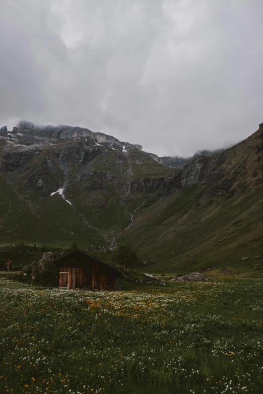 a small cottage nestled in a green field near the side of a mountain