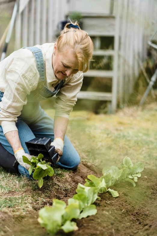 a woman is kneeling on the ground to plant leaves