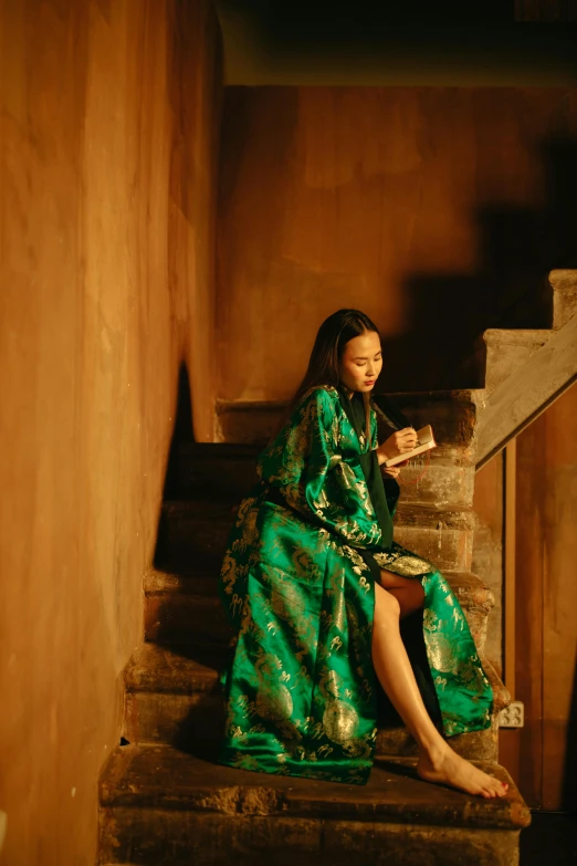 a woman in a long green dress sitting on a stair case