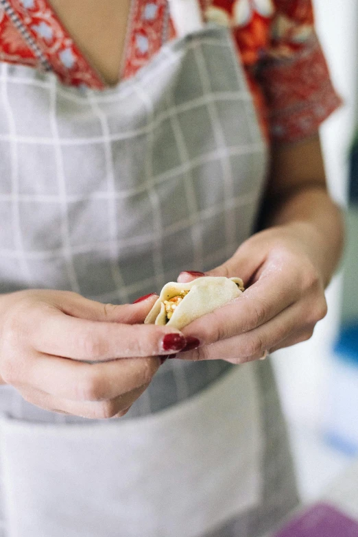 the woman is holding a small sandwich while she cooks