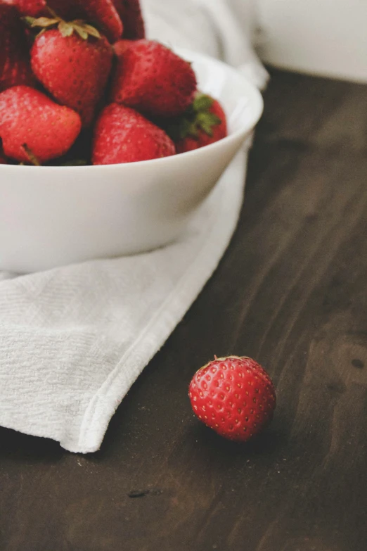 a white bowl filled with strawberries on top of a wooden table