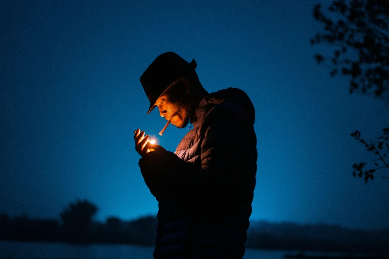 a man is standing in the dark holding a cigarette