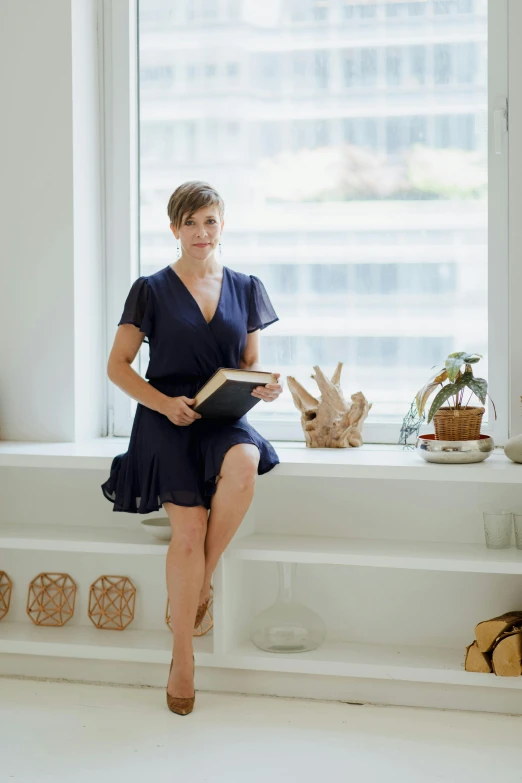 a woman in a short dress reading a book next to a window