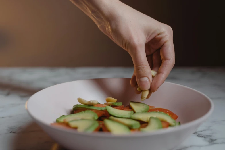 person putting a slice of cucumber in a white bowl