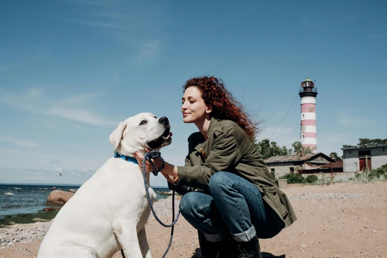 woman petting dog with lighthouse in background on beach