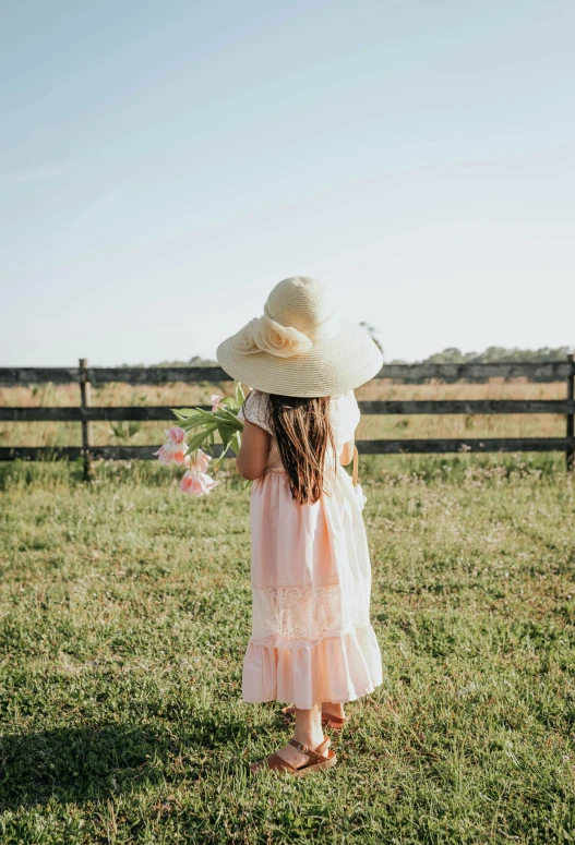 a girl is standing in the grass wearing a straw hat