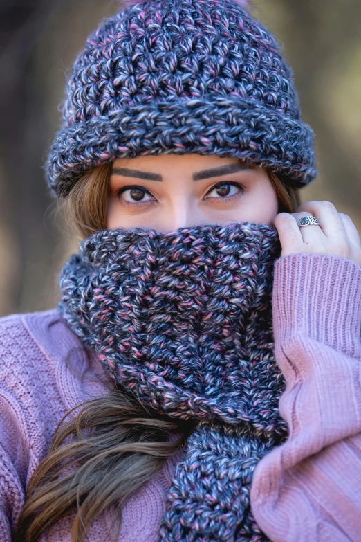 a woman in sweater and knit hat hides her face behind a scarf