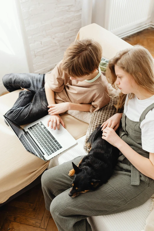 two young women looking at the laptop screen as a black dog stands next to them