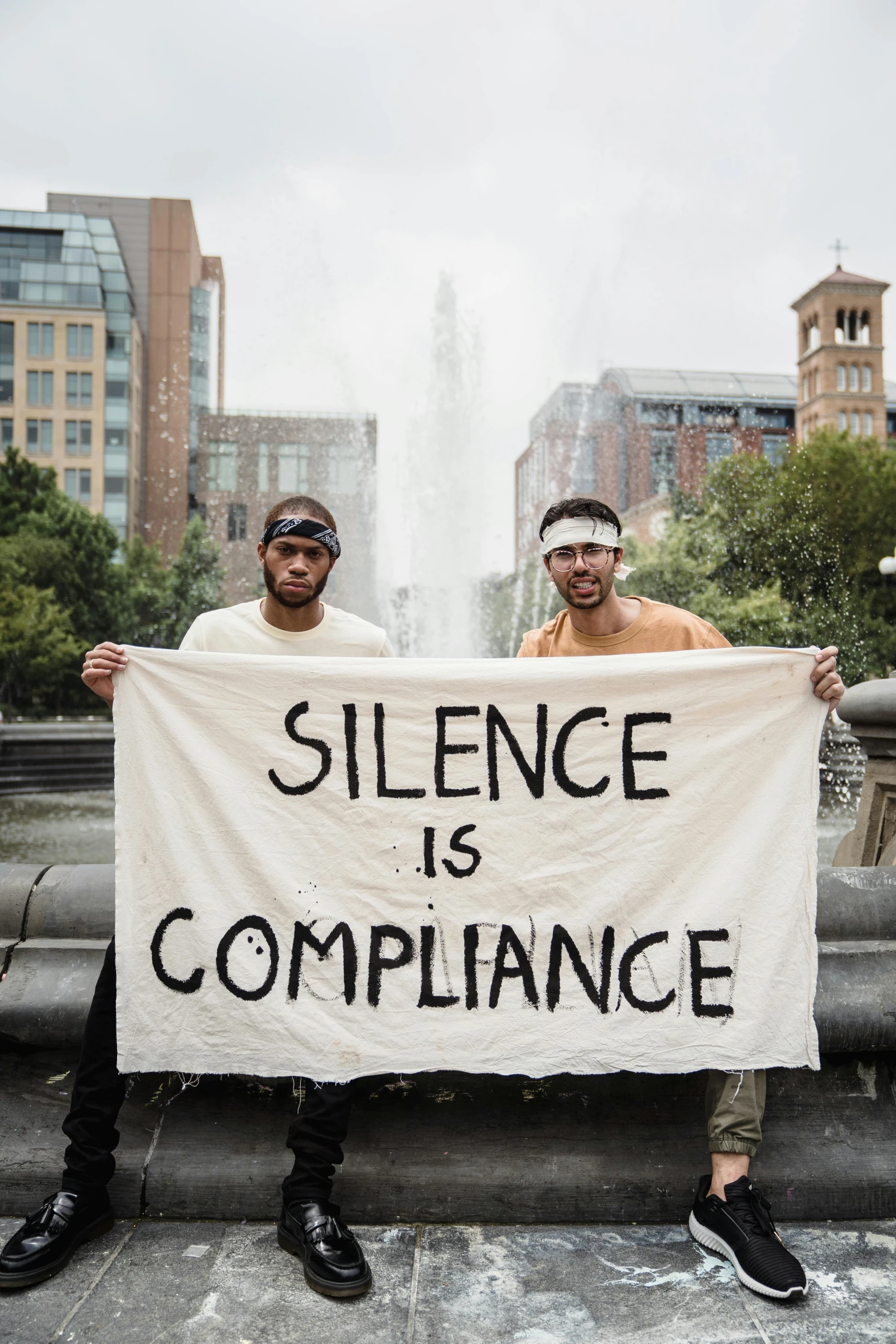 two men with glasses hold up a sign that says,'silence is compliance '