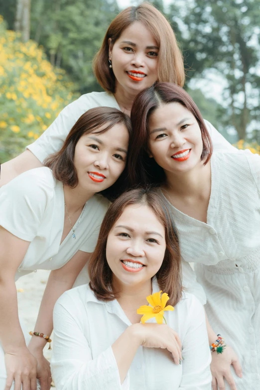 four asian women smile while posing in front of trees