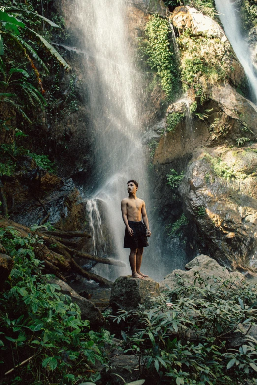 man stands in front of waterfall and looks up