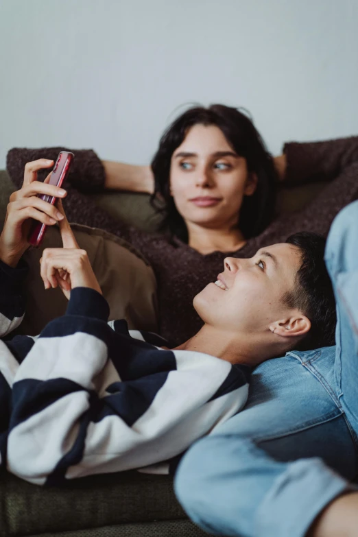 a man and woman are laying on the couch looking at a cell phone