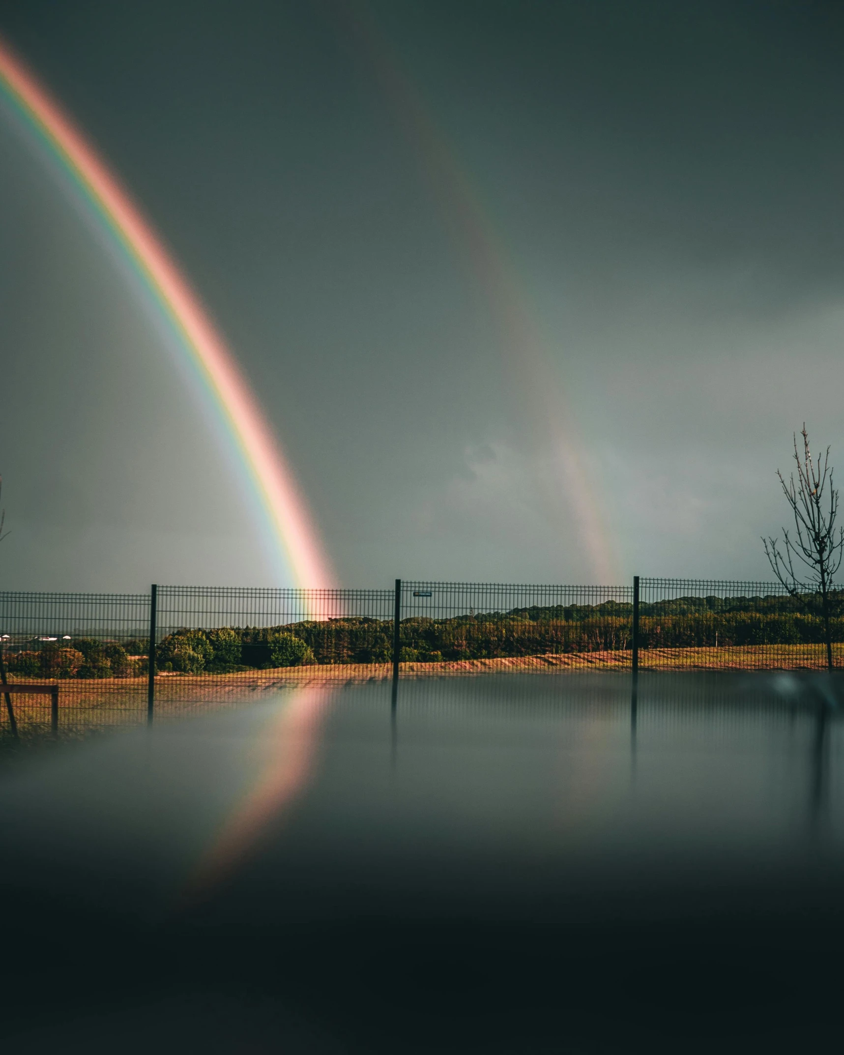 two rainbows shine brightly in front of a water fence