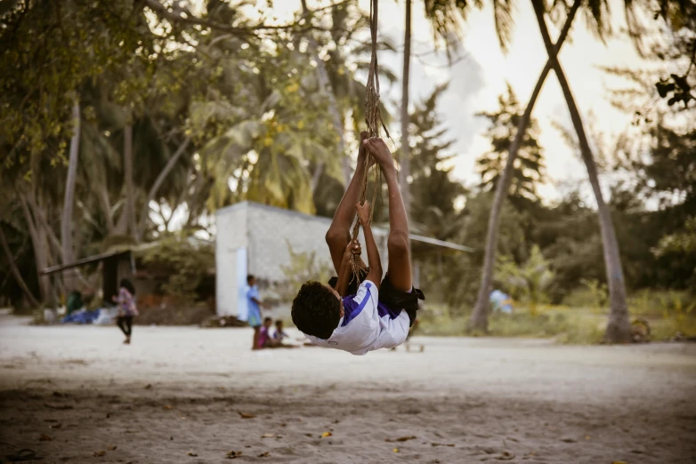 a child hangs upside down in a hammock between trees