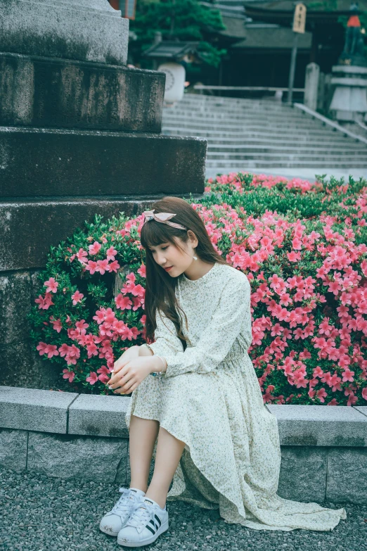 a girl in white dress sitting on the step near flowers