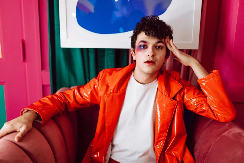 a man in an orange jacket sitting on a pink couch