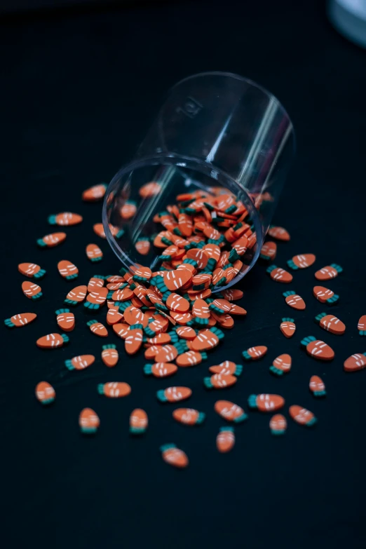 spilled orange pills sit in a clear cup on a black surface