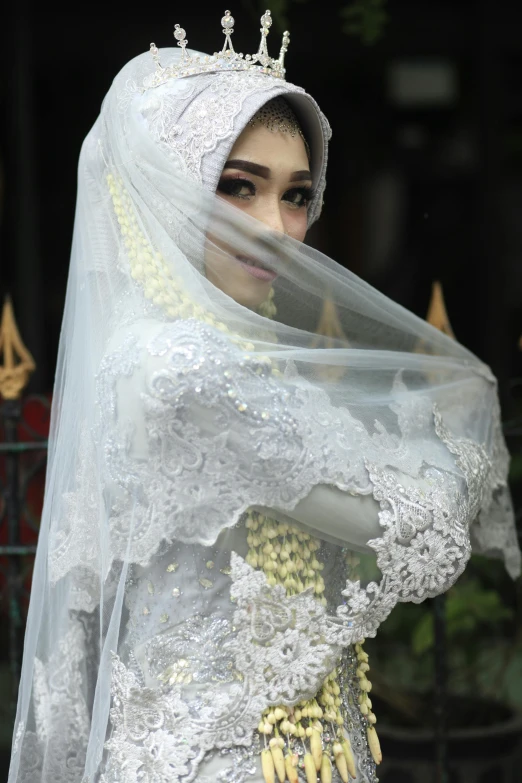 woman dressed in white and veil holding on to head