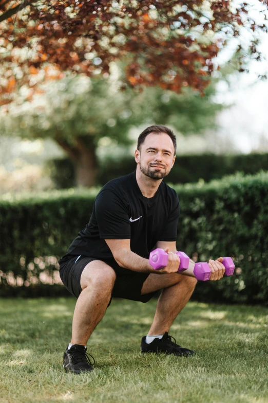 a man is lifting two purple dumbbells while crouching