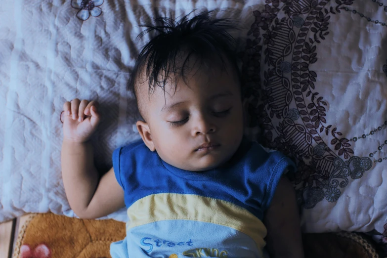 a baby sleeping on the bed with his hands up