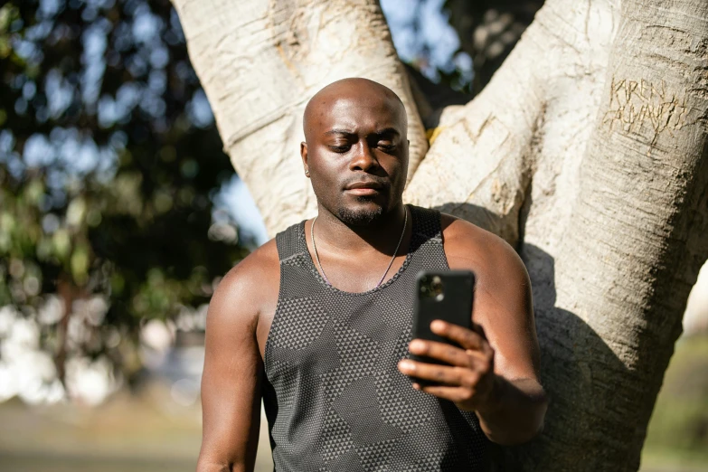 a man looking at his cellphone while standing in front of a tree