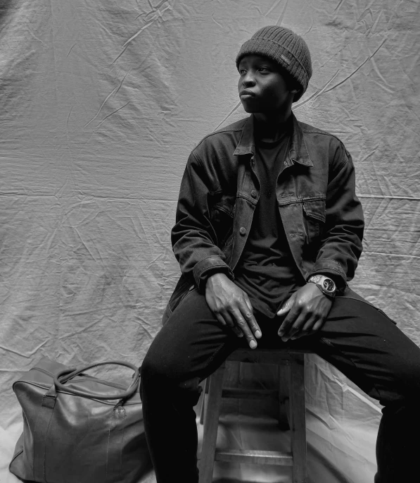 black man in denim jacket and hat sitting on stool