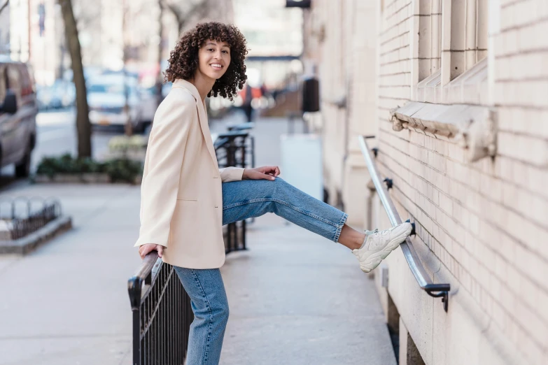 a smiling woman with curly hair leaning against a wall