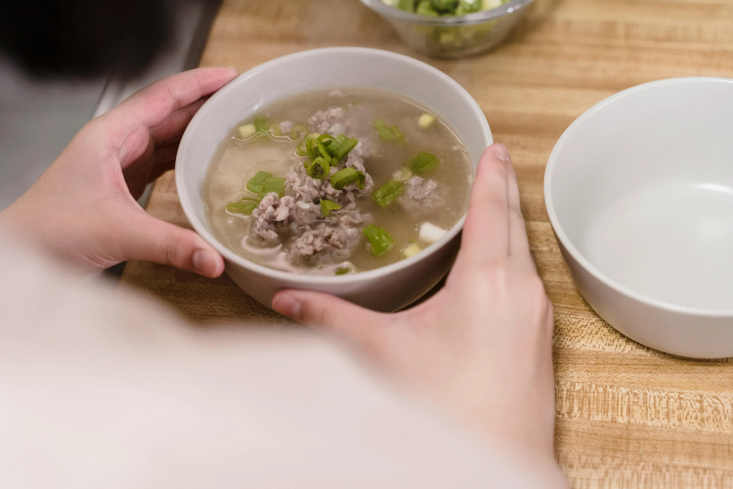 a person holding a bowl of soup with meat, celery and beans